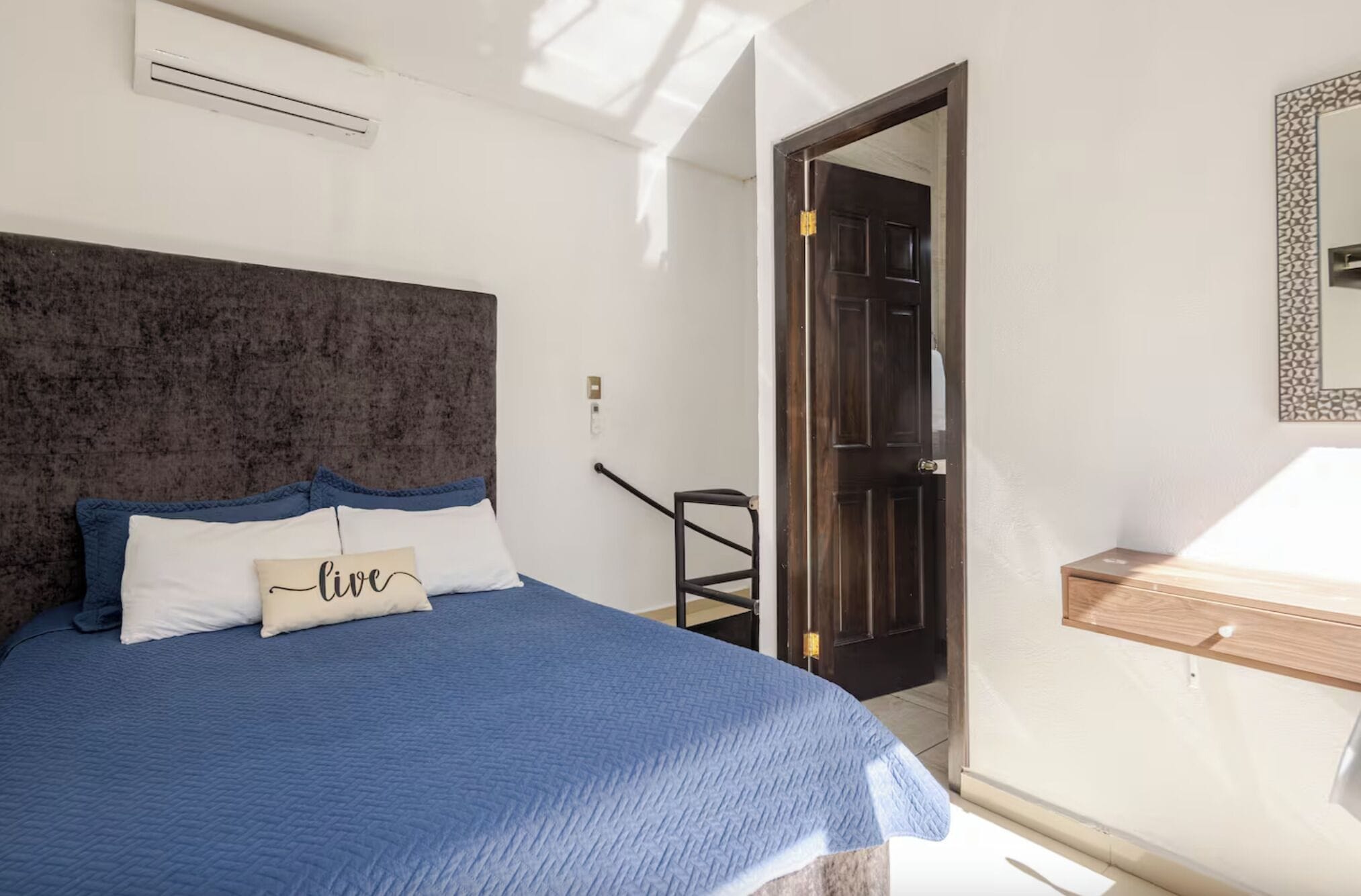 A bedroom with a large bed, a headboard, a bedside table, and a door leading to another room.