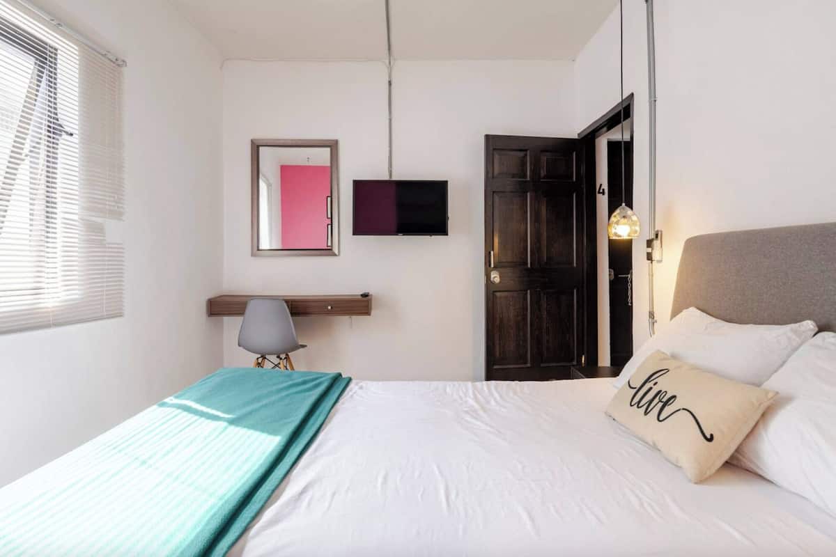 Un dormitorio con cama, escritorio, silla, televisión y puerta.