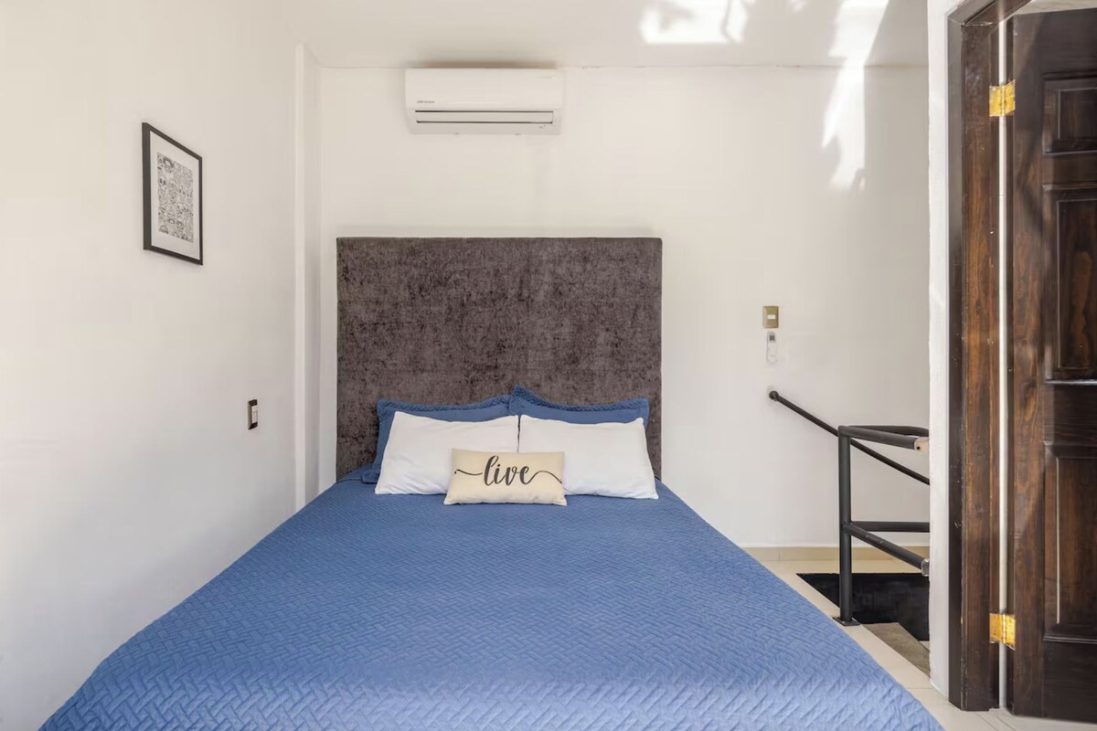 Een slaapkamer met een bed, hoofdeinde, airconditioning, een ingelijste foto en een deur.