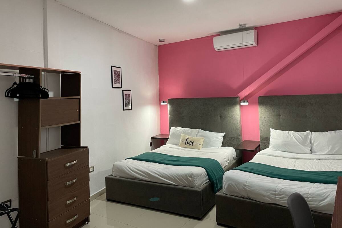 Un dormitorio con dos camas, un armario y una pared de acento color rosa.