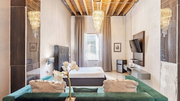 Una habitación de hotel moderna con una cama grande, un sofá verde, un televisor y una araña.