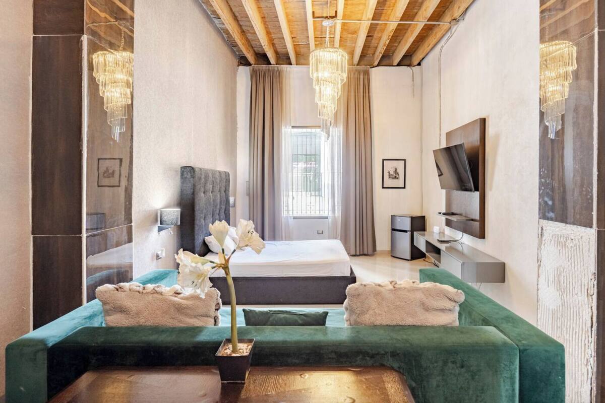 Una habitación de hotel moderna con una cama grande, un sofá verde, un televisor y una araña.