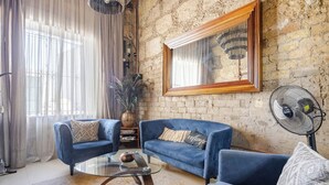 Una sala de estar con un sofá azul, una mesa de centro de vidrio, un espejo grande y un ventilador montado en la pared.