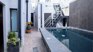 Un área de piscina moderna al aire libre con un muro de piedra, una escalera y plantas en macetas.