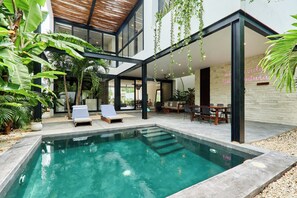 A modern outdoor pool area with lounge chairs, a dining area, and lush greenery. - Casa Aventura (Tulum)