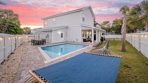 A white house with a swimming pool, outdoor furniture, and a hammock.