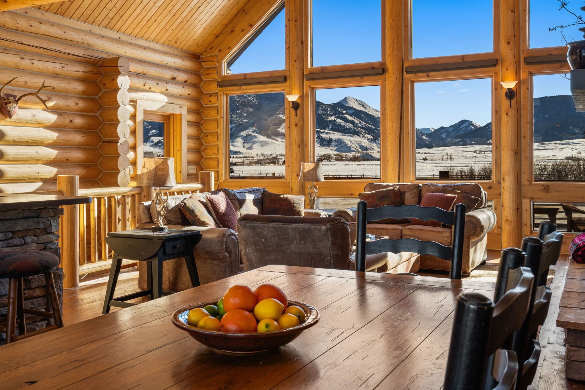 L’intérieur d’une cabane en rondins comprend un coin repas, une cheminée et de grandes fenêtres offrant une vue sur les montagnes.