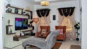 A living room with a sofa, armchair, TV, and decorative items. - Zinq Bridge Aparments (Abuja)