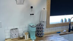 Een keuken met een houten aanrecht, een Keurig koffiezetapparaat, een rekje met kruiden en een raam met uitzicht op de omgeving.