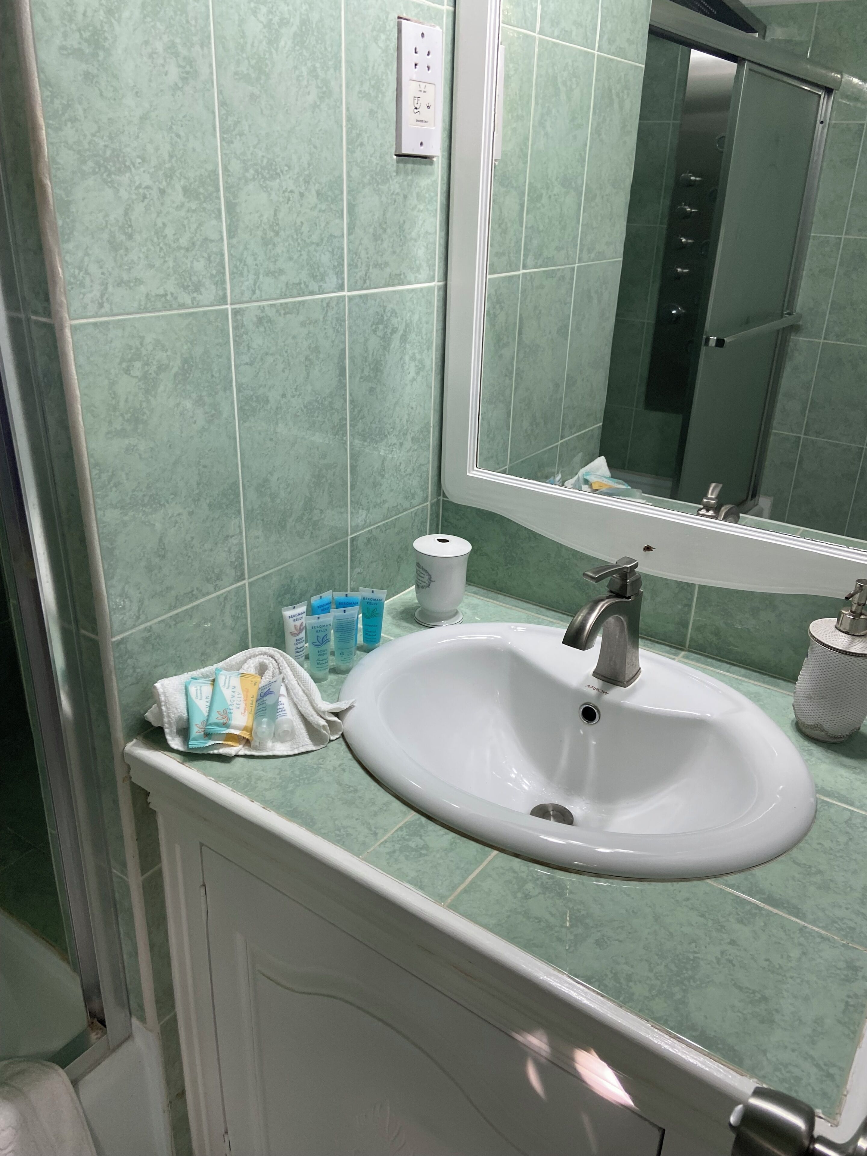 Une salle de bain avec un lavabo blanc, des carreaux verts, un miroir et des articles de toilette posés sur le comptoir.