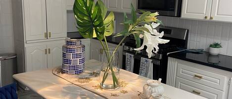 A modern kitchen with white cabinetry, a central island with a vase of flowers, and a blue upholstered chair.