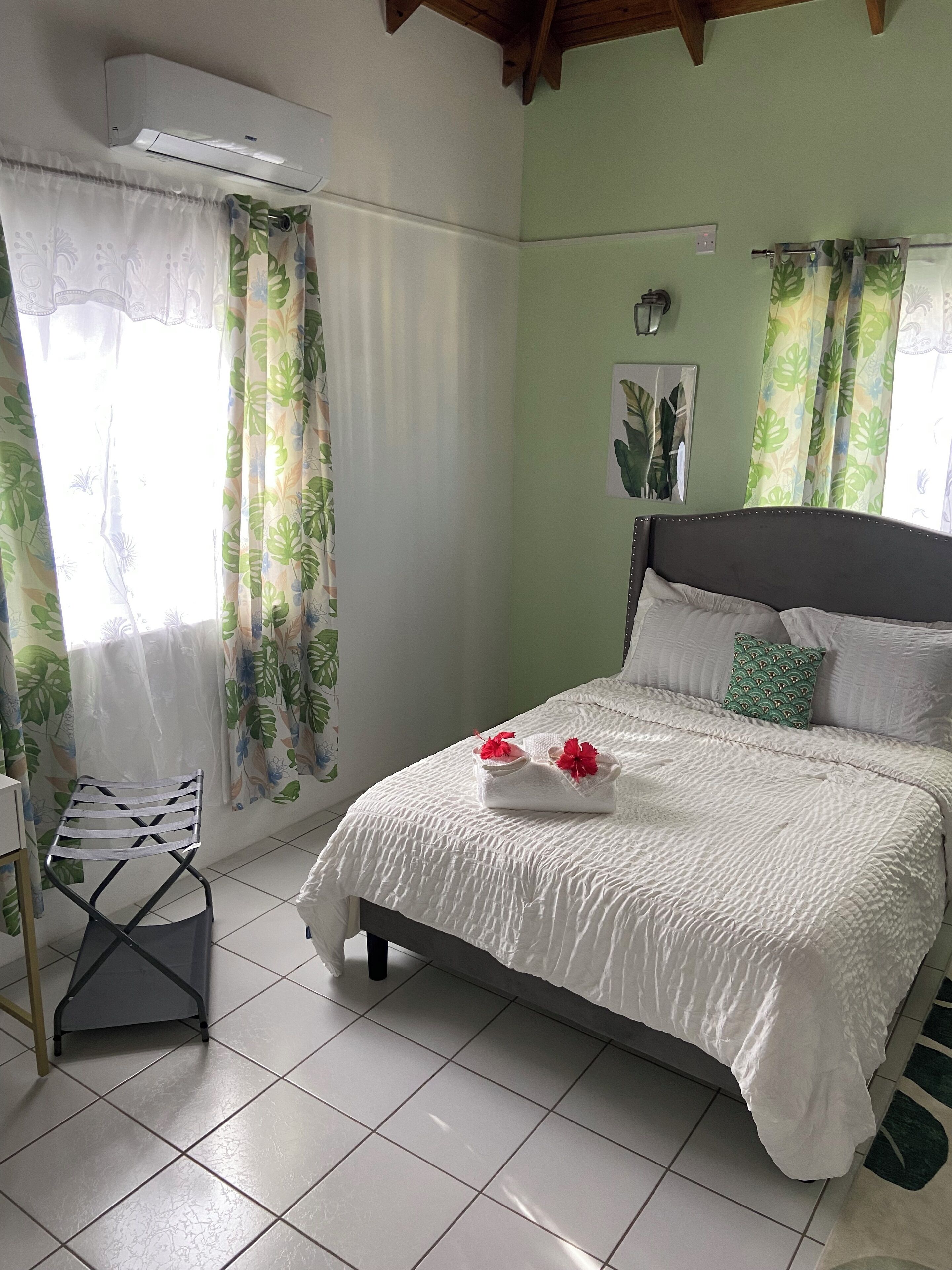 Una cama bien hecha con ropa de cama blanca y almohadas decorativas, una silla y un aire acondicionado de pared.
