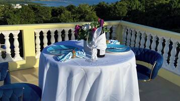 A table set outdoors with a view of the sea, a white tablecloth, and a bottle of wine.