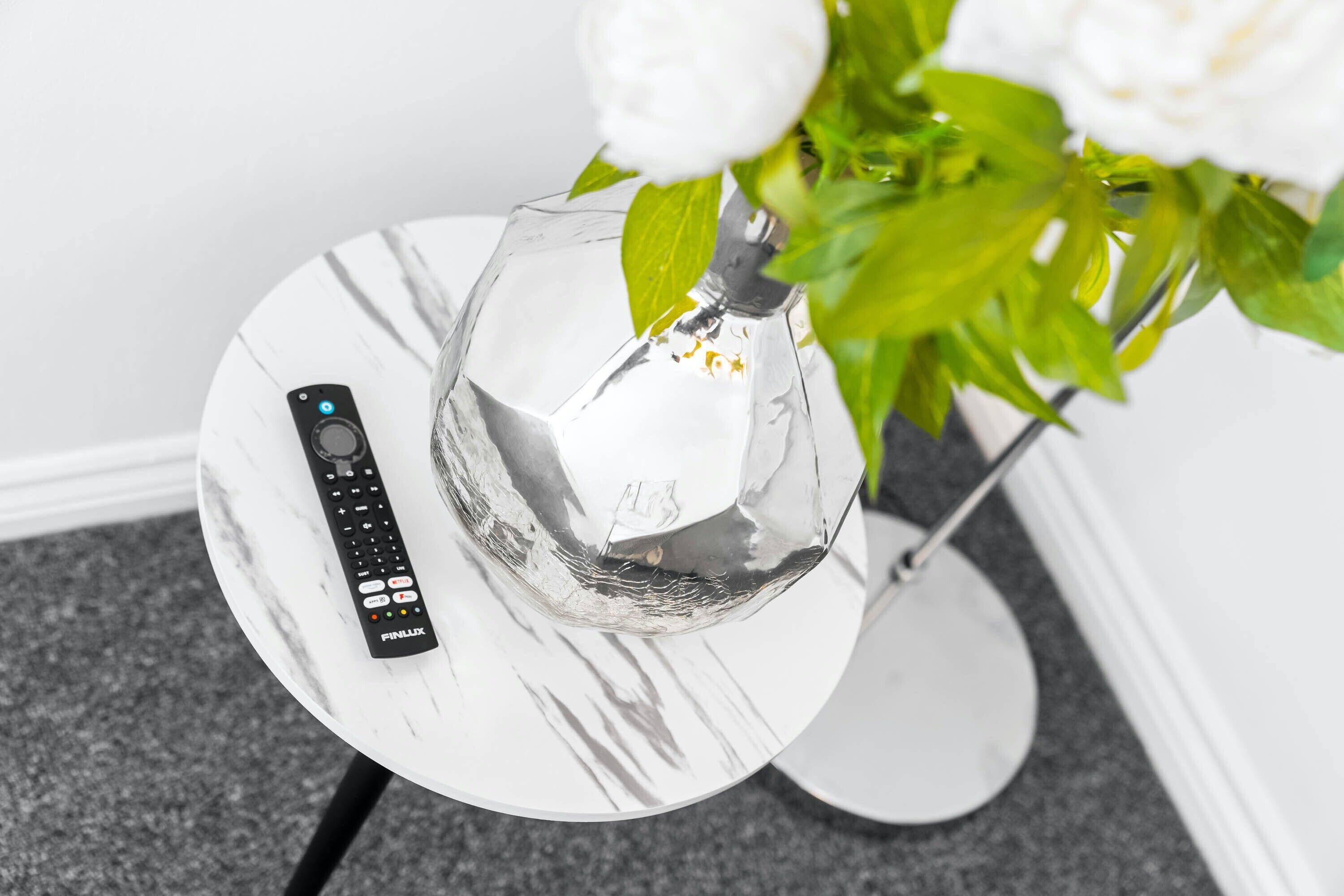 A clear glass vase on a white marble table with a remote control beside it.