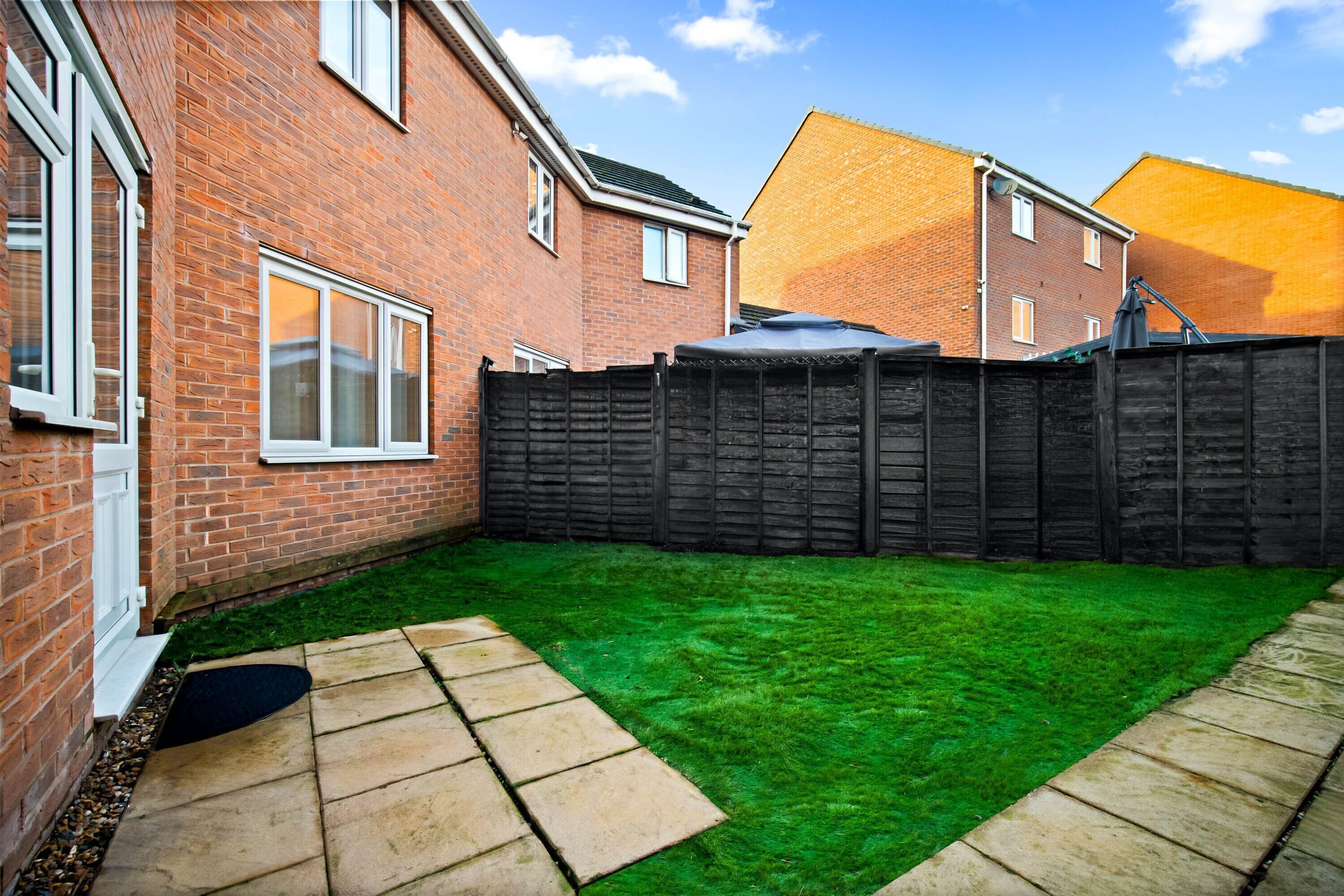 A backyard with a green lawn, a brick house, and a wooden fence.