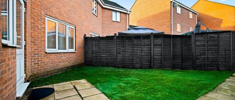 A backyard with a green lawn, a brick house, and a wooden fence.
