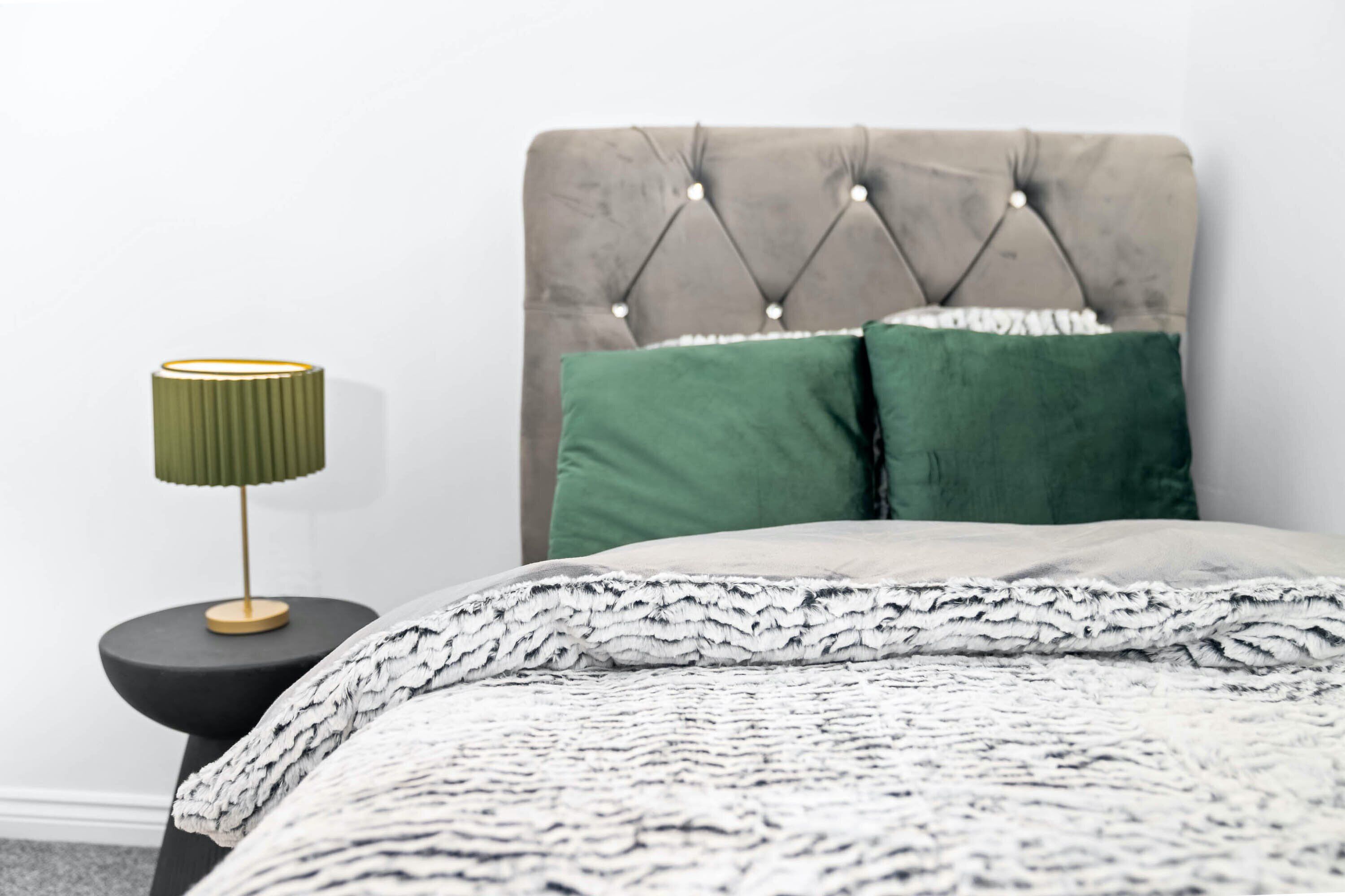 A neatly made bed with a tufted headboard, a green pillow, and a patterned blanket.