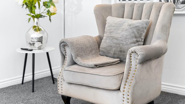 Un fauteuil moelleux avec un plaid à motifs, un vase de fleurs blanches et une petite table d’appoint.