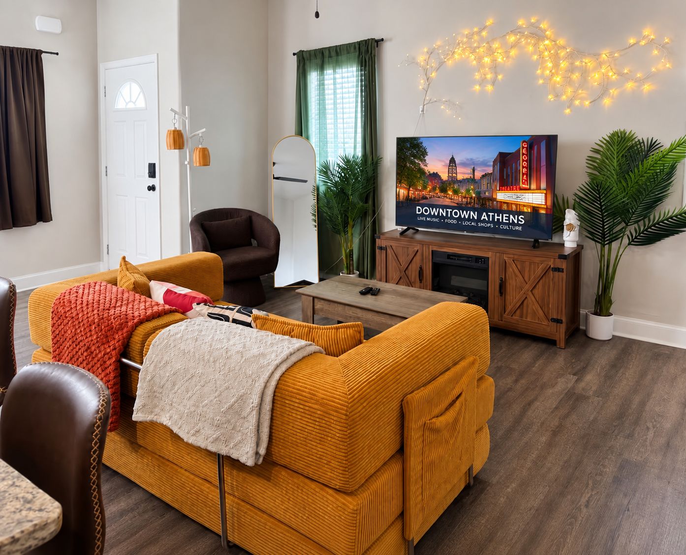Uma sala de estar com sofá, poltrona, televisão e planta.