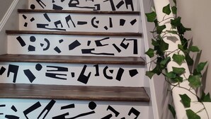 Eine Treppe mit Holzbodenstufen und weißen Verkleidungen mit schwarzen, abstrakten Mustern.