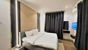 Ein modernes Hotelzimmer mit einem großen Bett, einem Nachttisch mit Telefon, einem an der Wand befestigten Fernseher und einem Fenster mit Vorhängen.