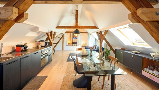 A spacious loft with high ceilings, exposed wooden beams, a kitchen with modern appliances, a dining area with a glass table, and skylights providing natural light. - Superb loft 10min from Strasbourg (Eckbolsheim)