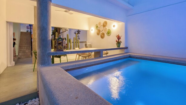 Un espace piscine intérieur moderne, offrant une vue dégagée sur le bassin, un coin salon avec des fauteuils et un mur décoratif orné de motifs circulaires.
