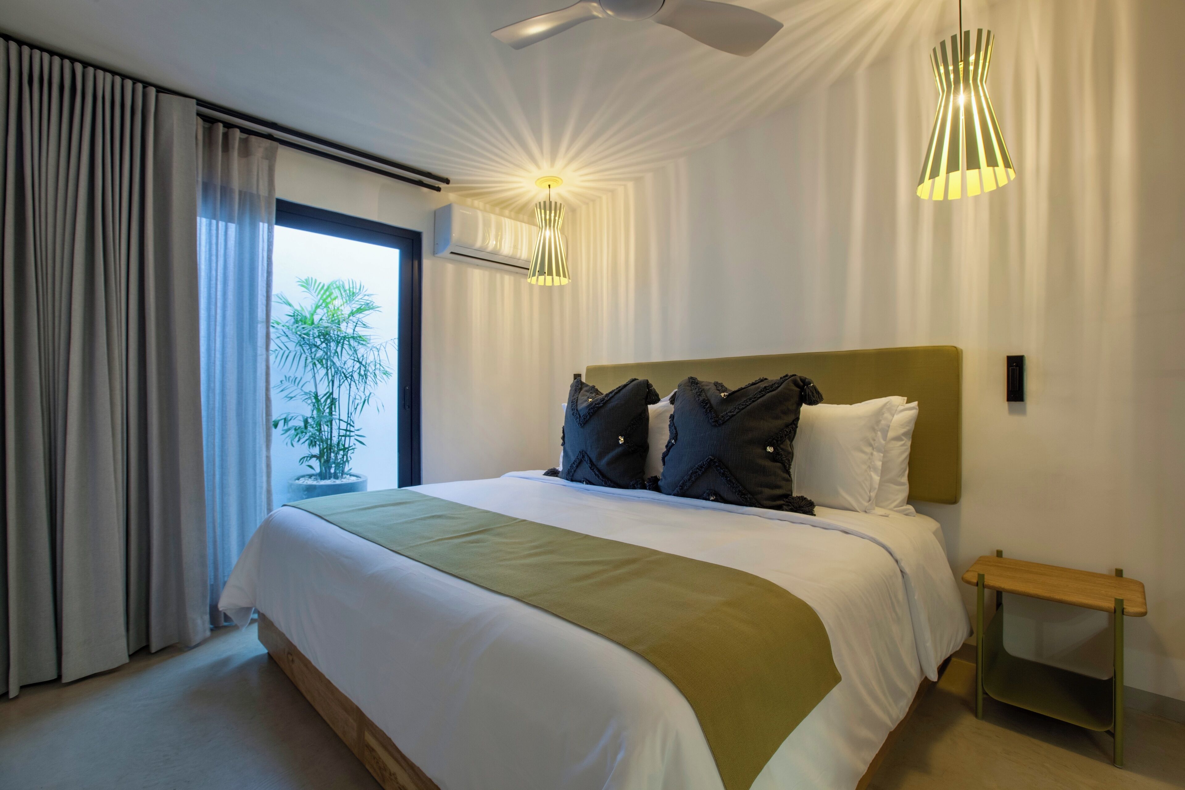 A modern hotel room with a large bed, a ceiling fan, and two pendant lights.