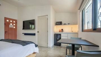 Una habitación de hotel compacta con una cama, una pequeña kitchenette, un comedor con mesa y sillas, y un televisor montado en la pared.