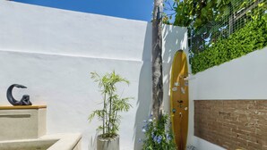Une cour avec un sol carrelé, une plante en bambou, une chaise jaune et une porte décorative.
