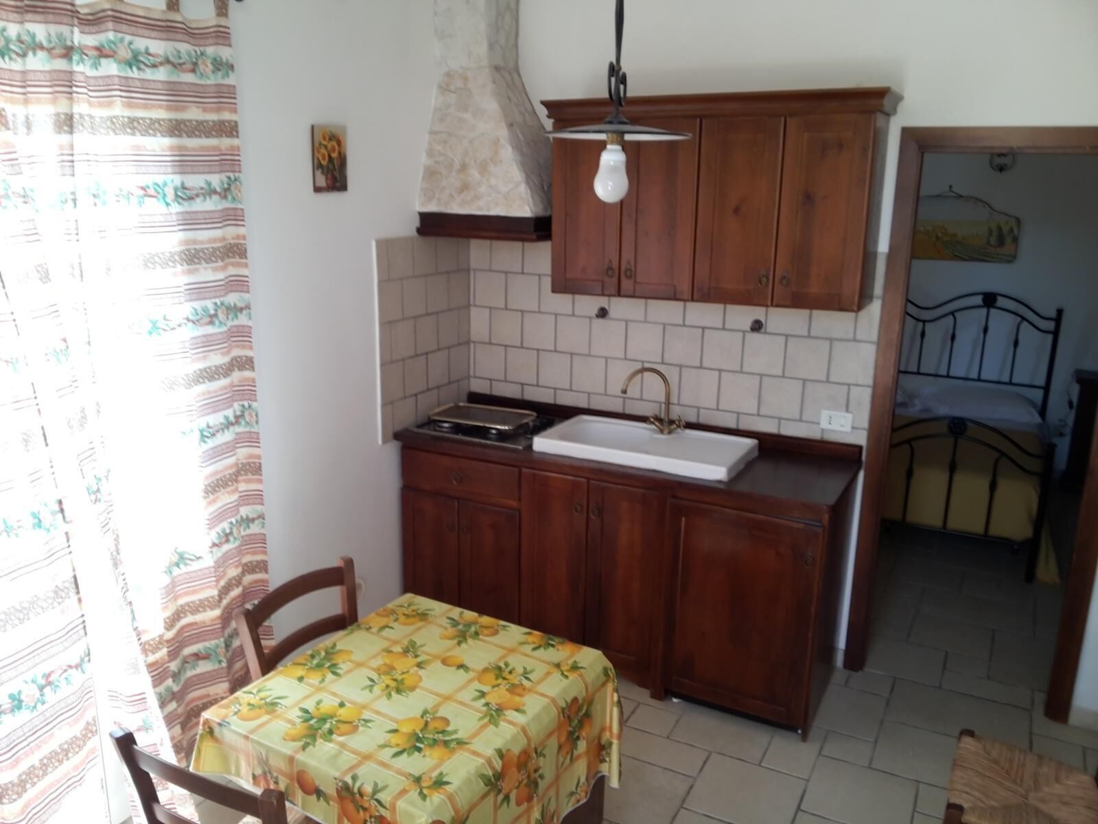 A compact kitchen with a sink, stove, and wooden cabinets. There is a dining table with a floral tablecloth.
