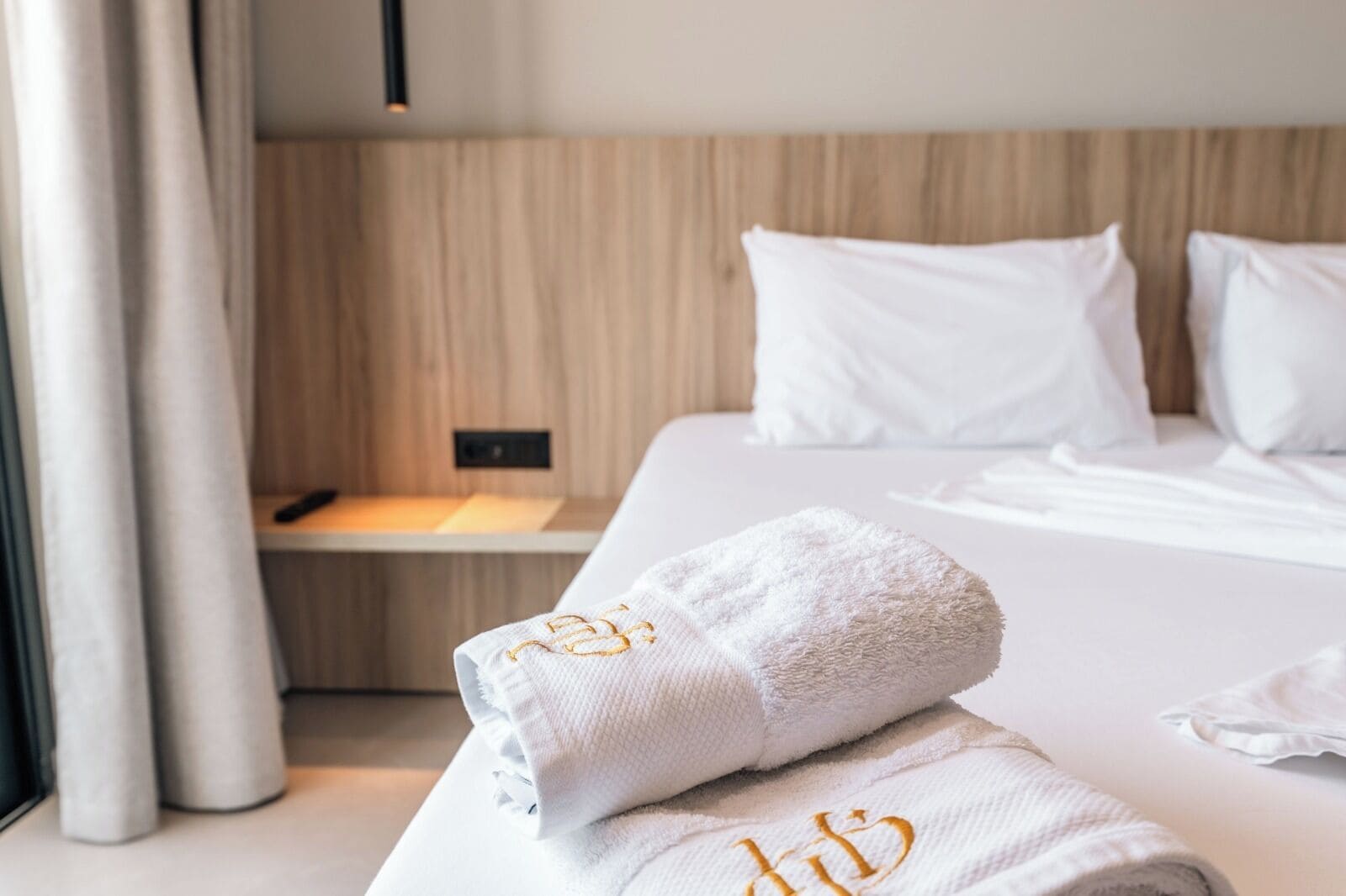 Un lit bien fait, avec du linge de lit blanc et des oreillers, une serviette blanche ornée de motifs brodés et une tête de lit en bois.