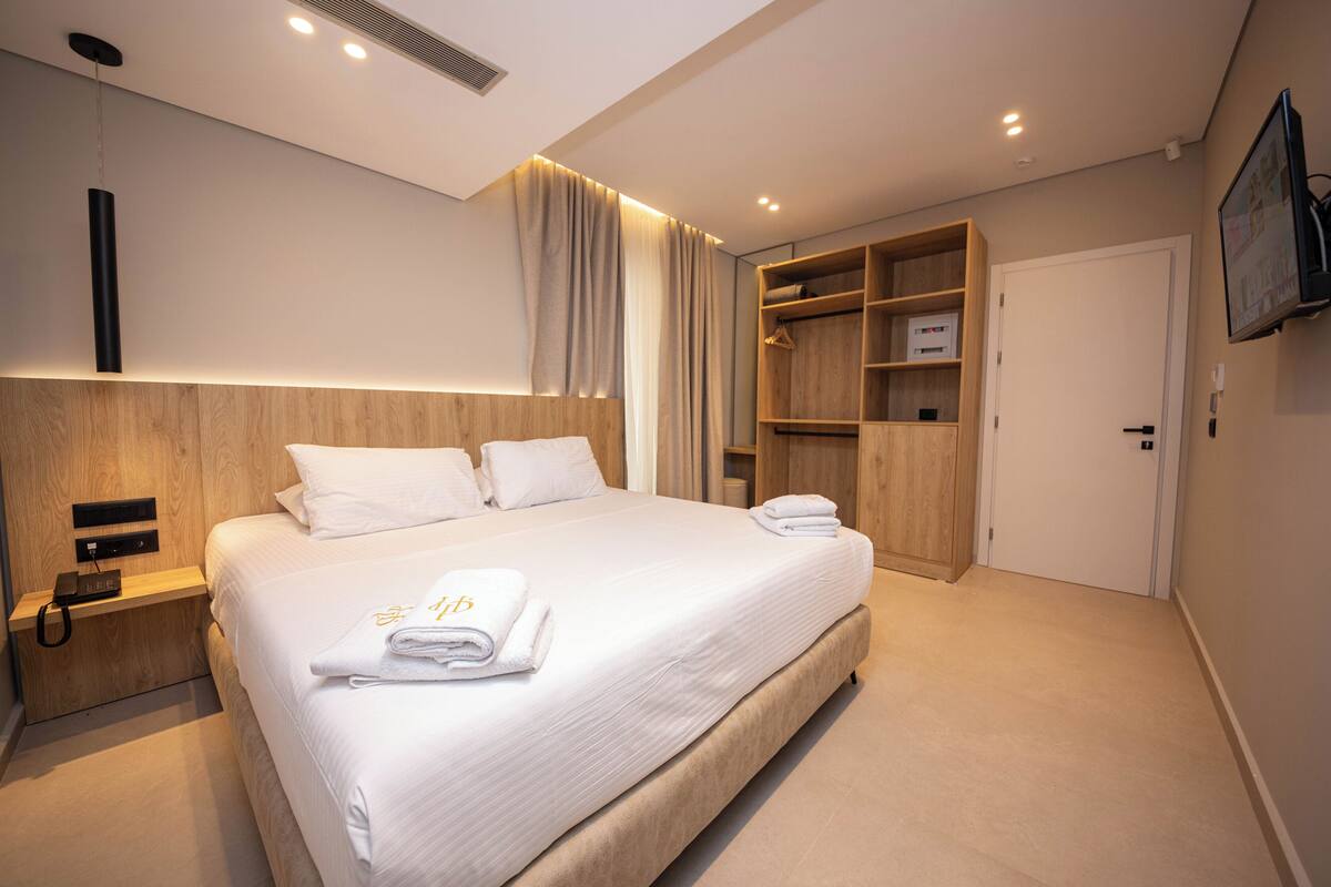 Une chambre d’hôtel moderne, dotée d’un grand lit, d’un téléphone sur la table de chevet, d’une armoire et d’un téléviseur fixé au mur.