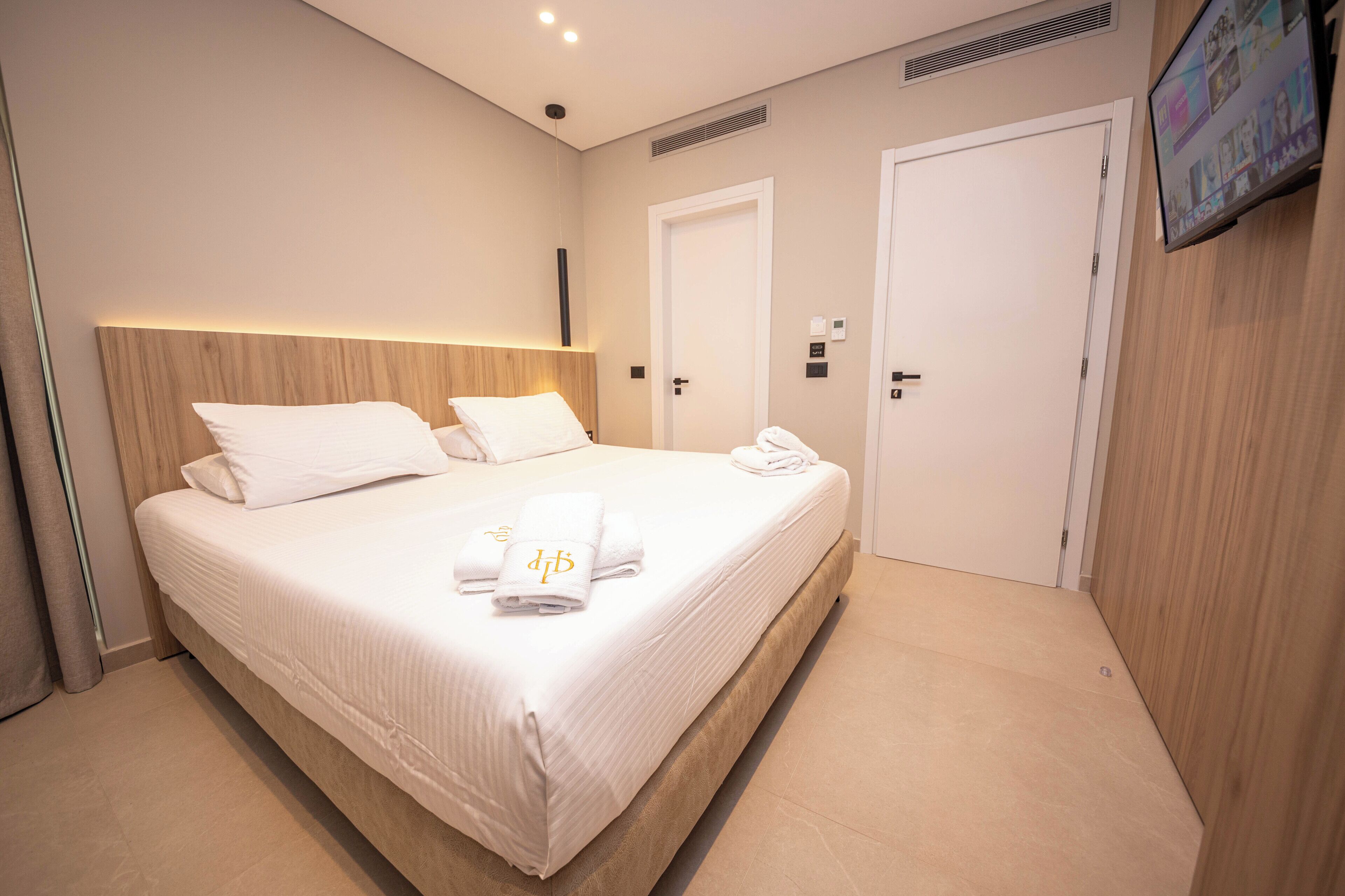 Ett hotellrum med en stor säng, en sänggavel i trä, en platt-TV som är monterad på väggen och en dörr med ett lås som öppnas med en kod.