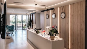A modern reception area with a reception desk, potted plants, and clocks on the wall. - Hotel Portanova (Sarandë)