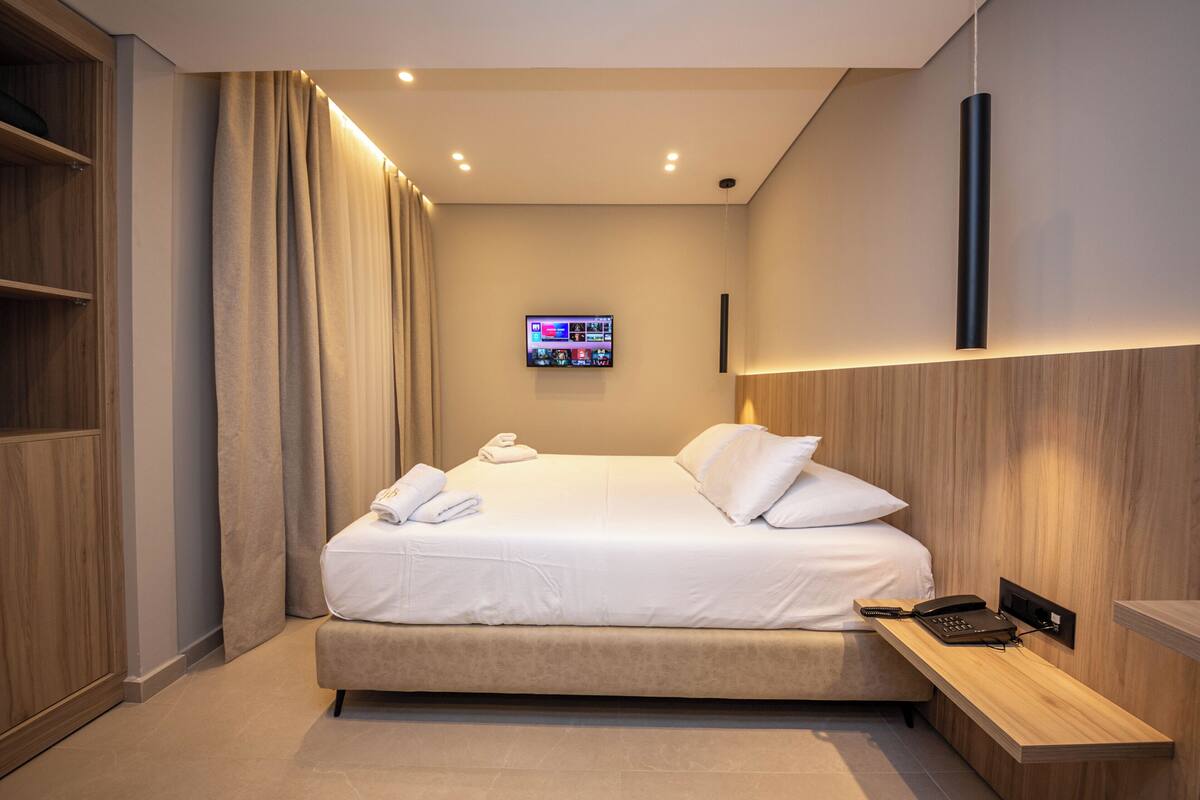 Une chambre d’hôtel moderne équipée d’un lit, d’un téléviseur fixé au mur et d’une table de chevet avec un téléphone et une lampe.