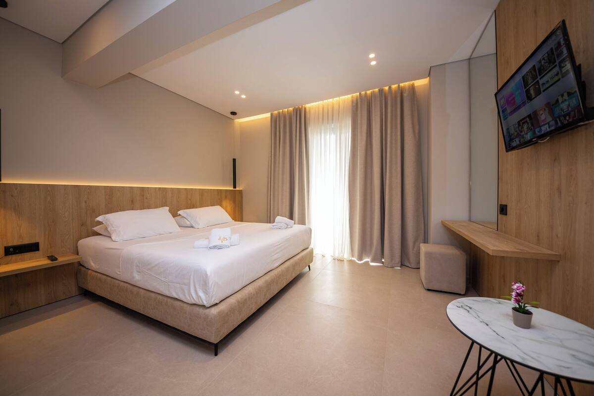 Une chambre d’hôtel moderne avec un grand lit, des tables de chevet, une petite table sur laquelle est posée une plante en pot et un téléviseur fixé au mur.