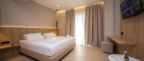 Una habitación de hotel moderna con una cama grande, mesitas de noche, una pequeña mesa con una planta en maceta y un televisor montado en la pared.