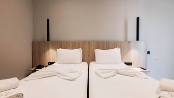 Habitación de hotel con dos camas, cada una con cabecero de madera, ropa de cama blanca y un control remoto en la mesita de noche.
