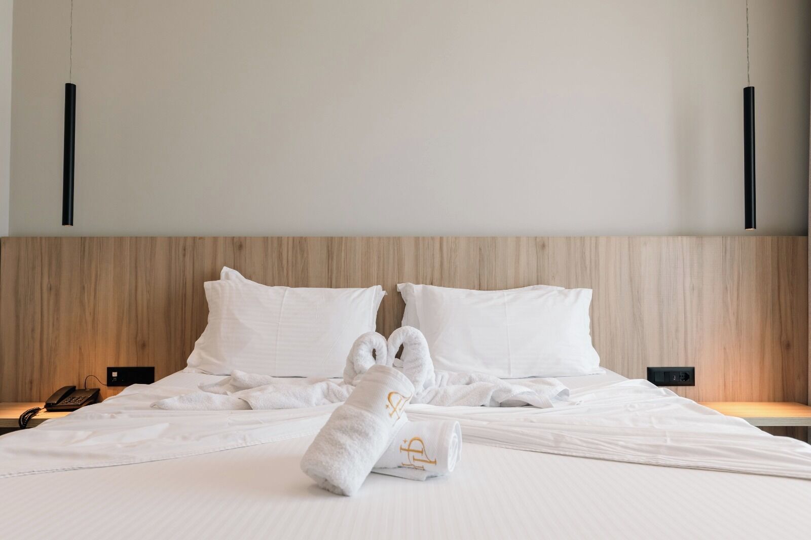 A neatly made bed with white linens and two towels folded in the center.