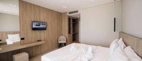 A modern hotel room with a large bed, a TV mounted on the wall, a wooden wardrobe, and a small seating area.