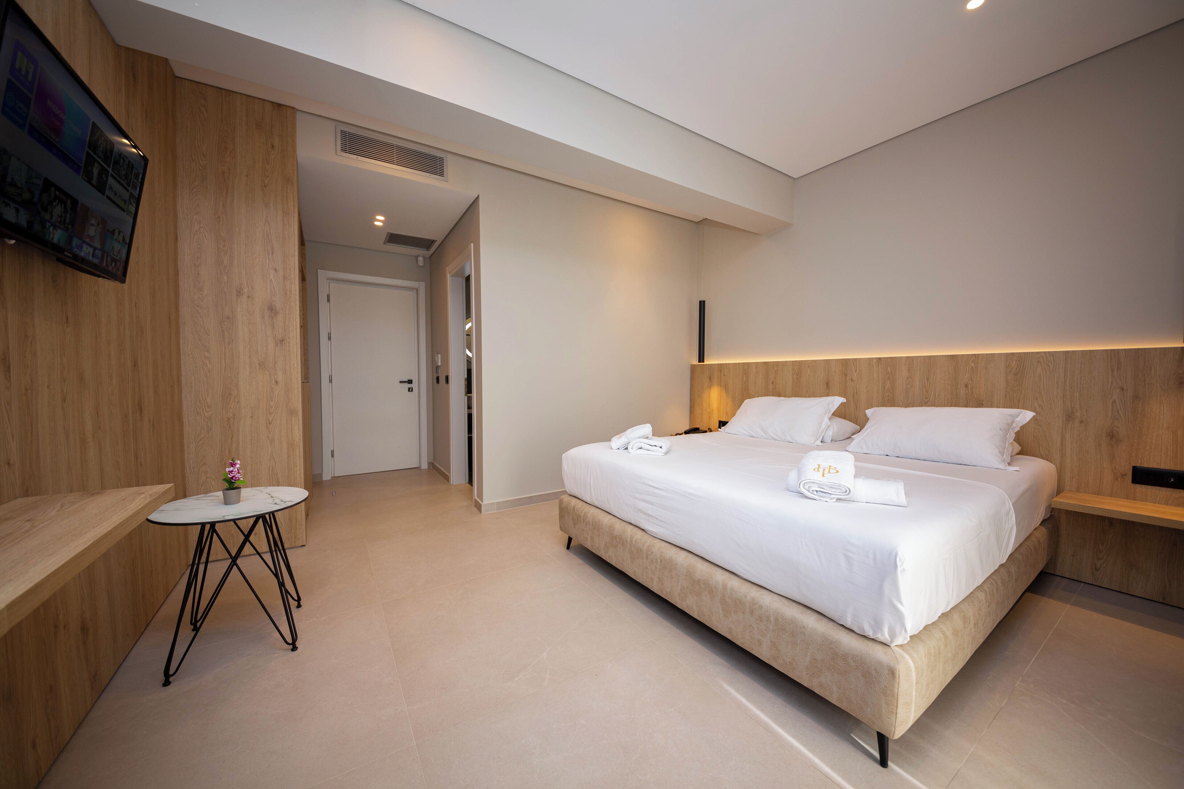 A modern hotel room with a large bed, a small round table, and a TV mounted on the wall.