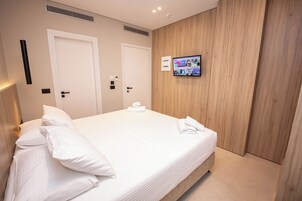 A modern hotel room with a large bed, two doors, a mounted TV, and a wooden accent wall.