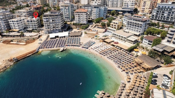 An aerial view of a coastal area with a beach, hotel buildings, and a marina. - Hotel Portanova (Sarandë)