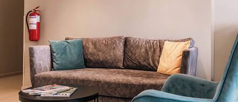 A modern lobby with a grey sofa, a blue armchair, a round coffee table, and a painting of a beach scene.