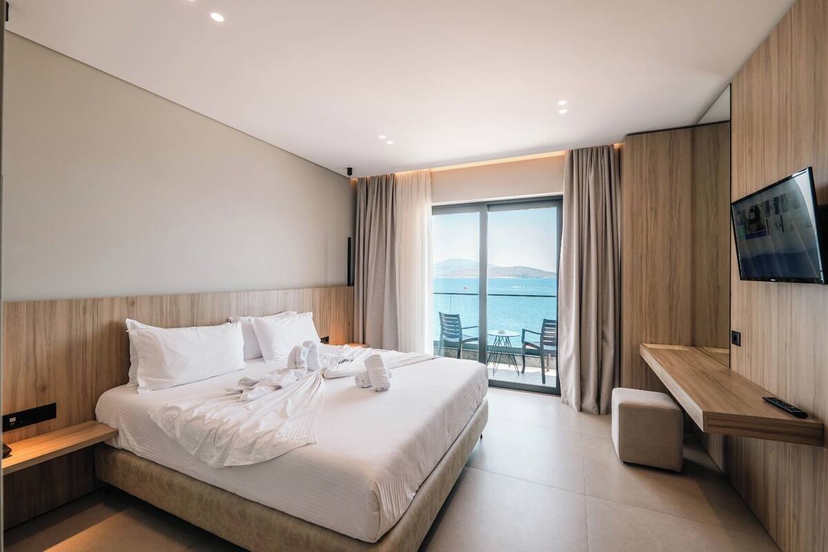Une chambre d’hôtel moderne dotée d’un grand lit, d’un bureau, d’une télévision et d’un balcon offrant une vue sur la mer.