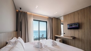 A hotel room with a large bed, a TV mounted on the wall, and a view of the sea through the window. - Hotel Portanova (Sarandë)