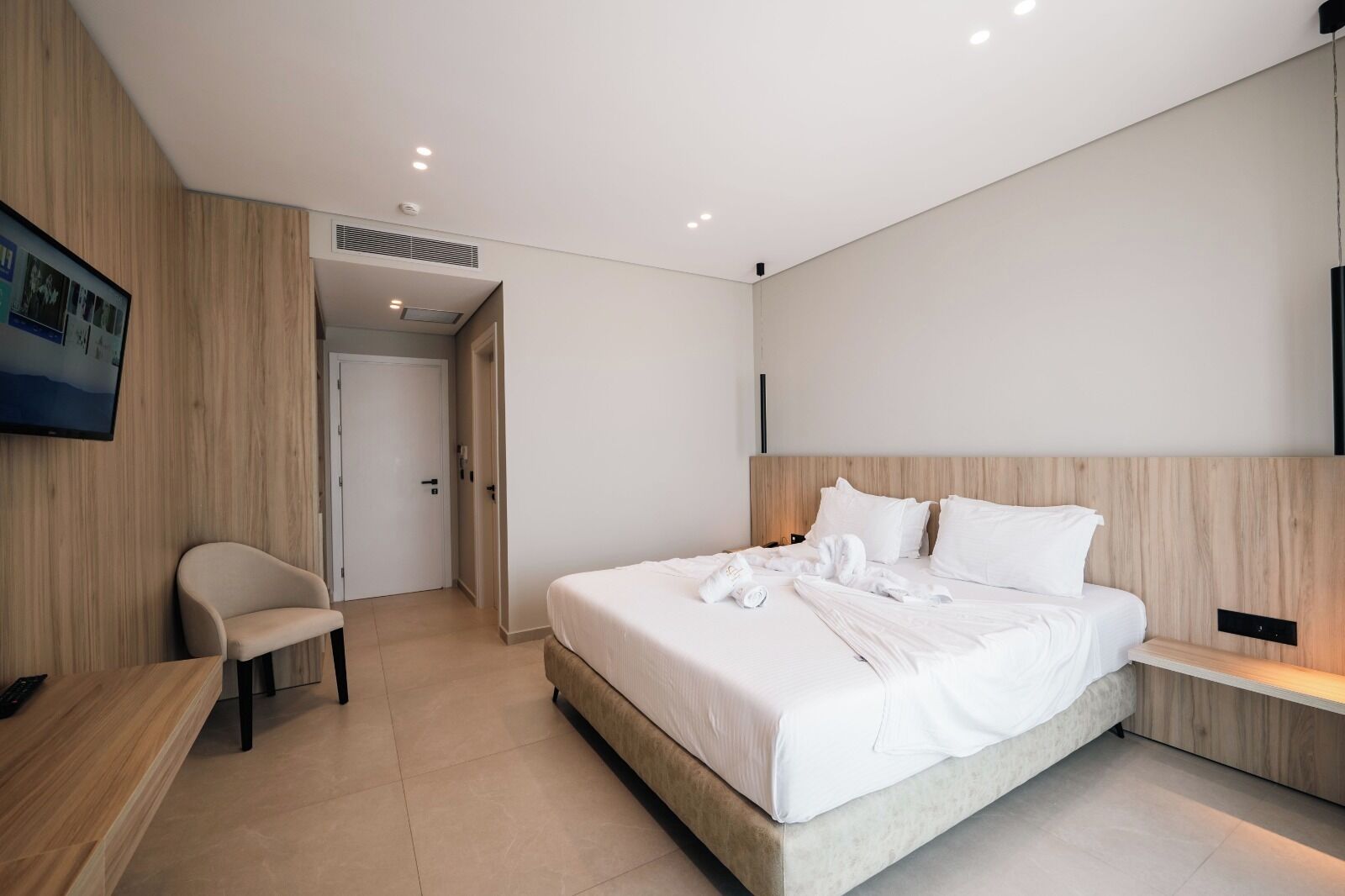 A modern hotel room with a large bed, a desk, and a television on the wall.