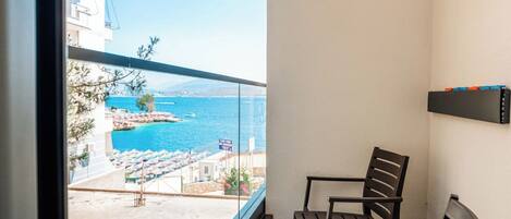 A balcony with a view of a beach and sea, a table with chairs, and a shelf with items.