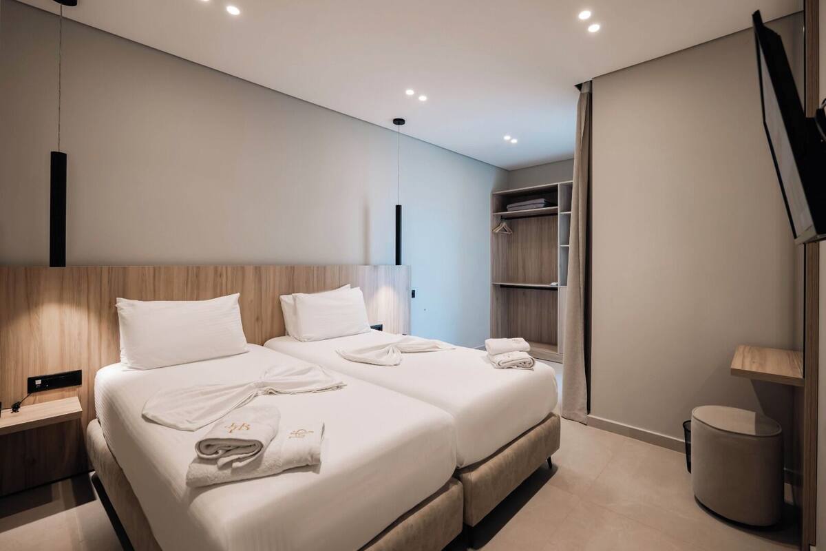 Une chambre d’hôtel moderne équipée de deux lits, d’une armoire, d’une table de chevet et d’une poubelle.